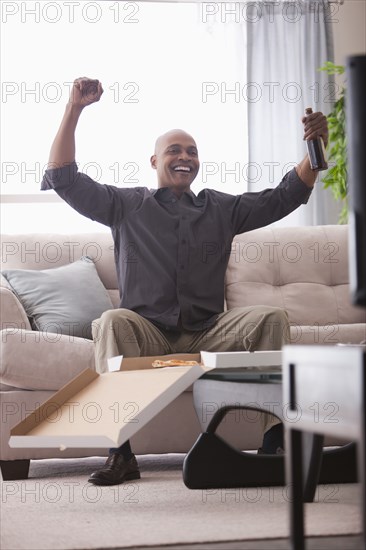 Black man cheering at television and eating pizza