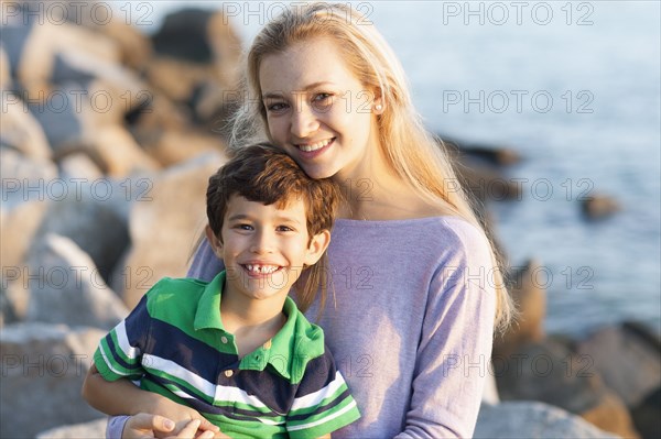 Caucasian brother and sister smiling on rocky beach