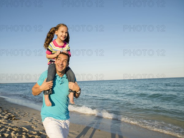 Hispanic father carrying daughter on shoulders on beach