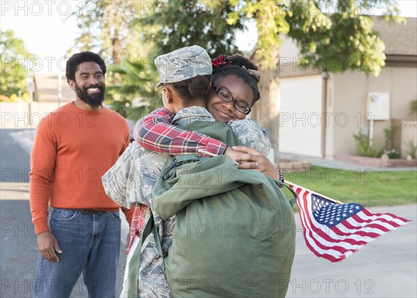 Man watching black woman soldier hugging daughter