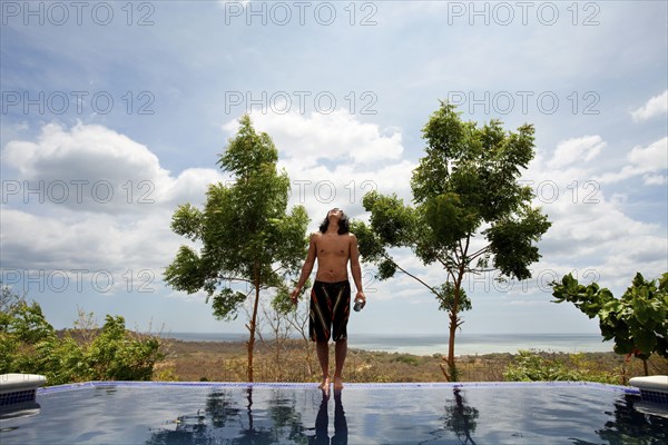 Asian man standing on edge of infinity swimming pool