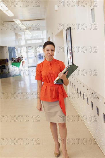 Mixed race teacher holding clipboard in school hallway