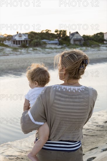 Caucasian mother holding baby on beach