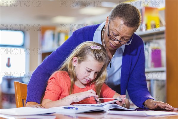 Teacher helping student use digital tablet in library