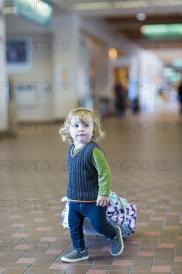 Caucasian baby boy rolling luggage in airport