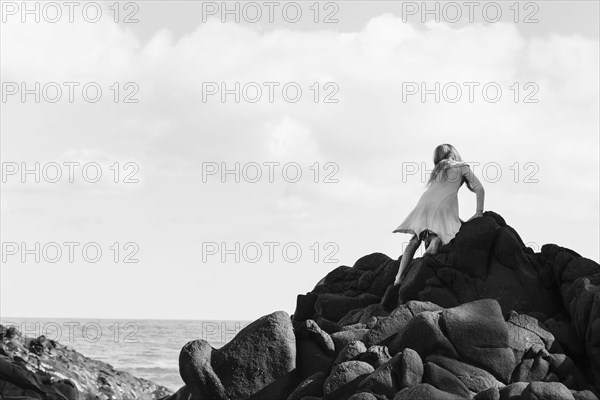 Caucasian girl climbing rocks at beach