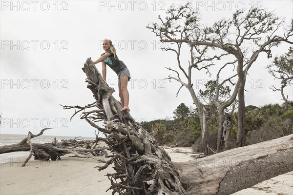 Caucasian girl climbing on driftwood on beach