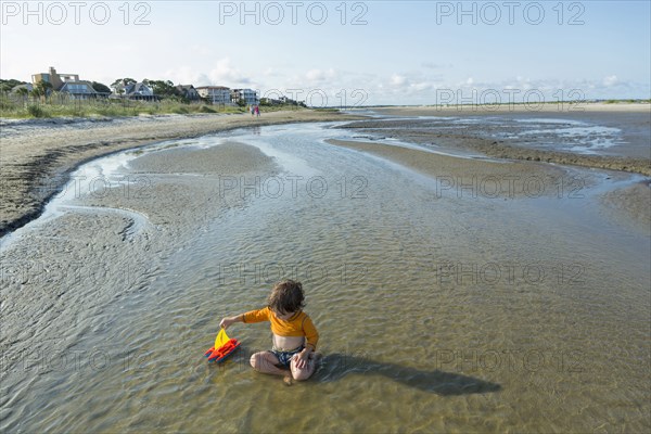 Caucasian boy playing with sailboat in waves on beach