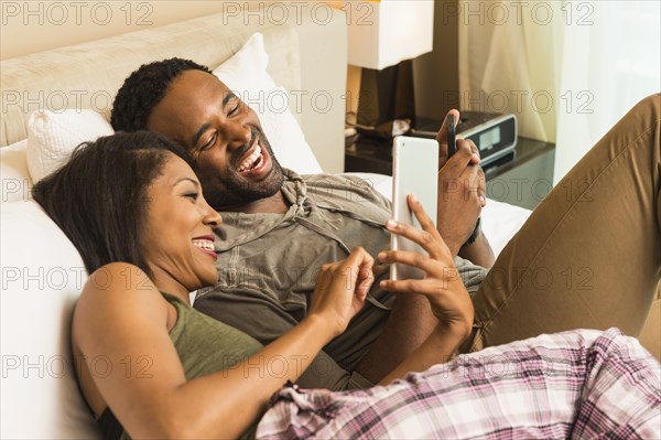 Couple using digital tablet on bed