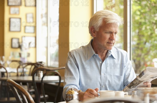 Caucasian man reading newspaper in restaurant