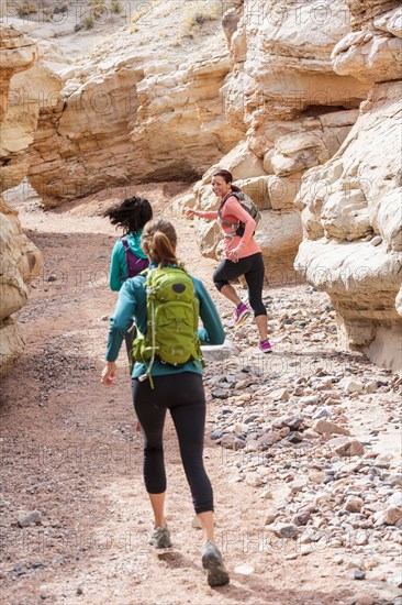 Women running in canyon wearing backpacks