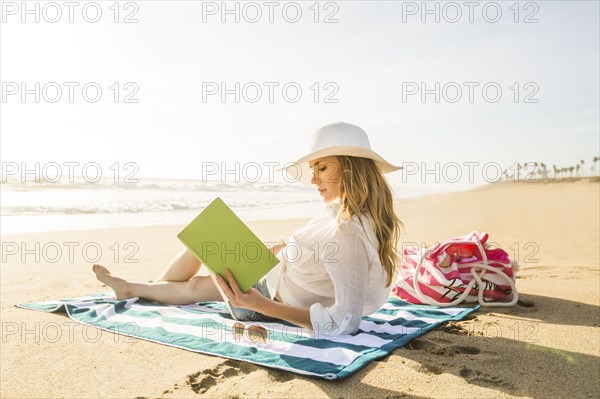 Caucasian woman reading book on beach