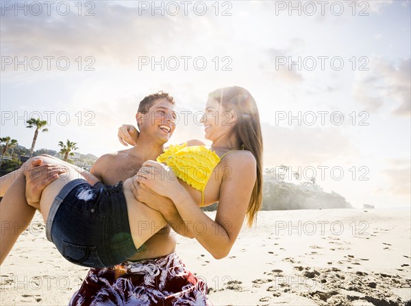 Caucasian man carrying girlfriend on beach