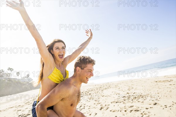 Caucasian man carrying girlfriend on beach