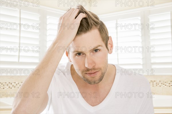 Serious Caucasian man styling hair in bathroom