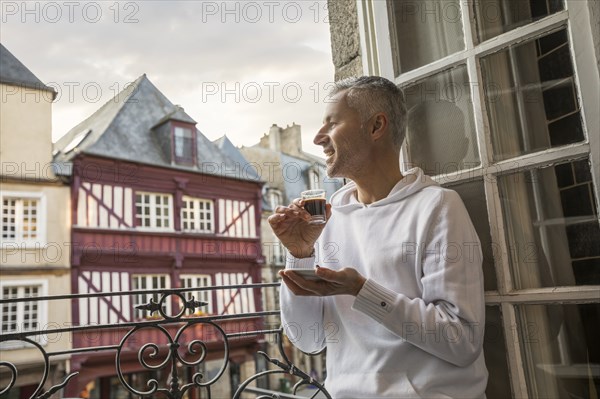 Caucasian man enjoying espresso on balcony in city