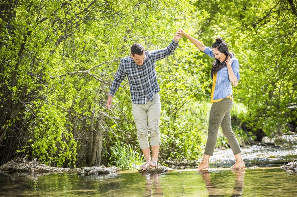 Man helping woman standing on rocks crossing river