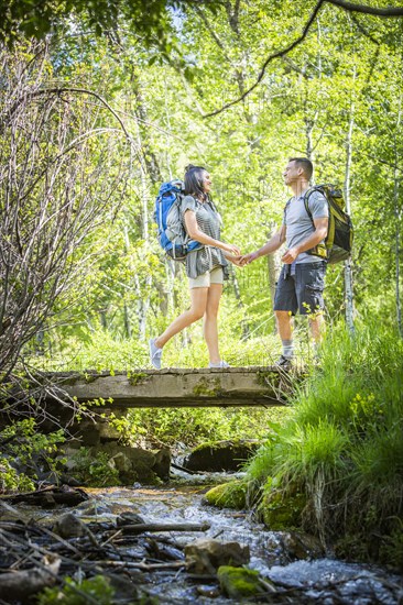 Couple carrying backpacks across bridge in woods