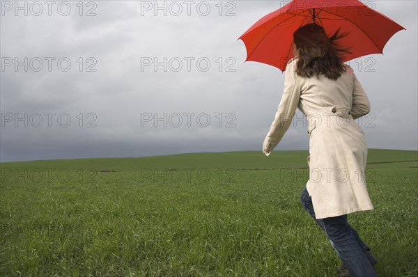 Rear view of woman running with umbrella in field