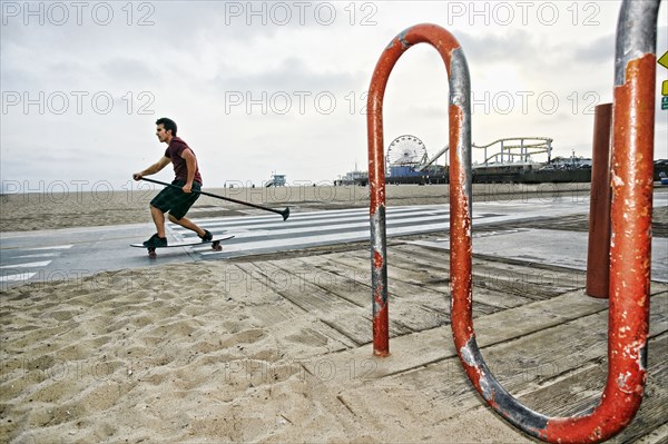 Caucasian man skateboarding with paddle pole at beach