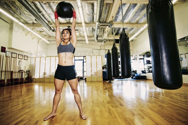 Asian woman lifting heavy ball in gymnasium