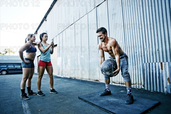 Women watching man lifting heavy ball outdoors