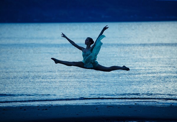 Caucasian ballerina jumping on beach at sunset