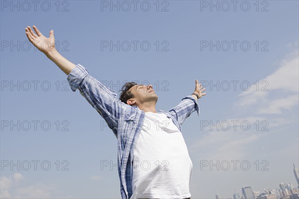 Hispanic man standing with arms outstretched against blue sky