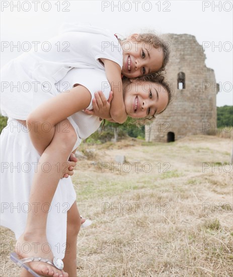 Hispanic girl giving sister piggyback ride near castle ruins