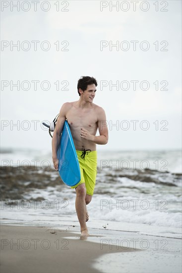 Hispanic man carrying surfboard on beach