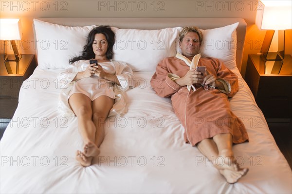 Couple using cell phones on bed
