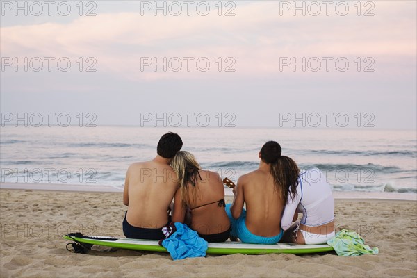 Teenage couples sitting on surfboard on beach
