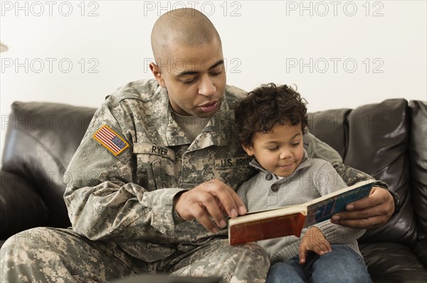 Mixed race soldier reading book to son on sofa