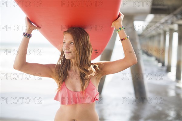 Woman carrying surfboard under boardwalk on beach