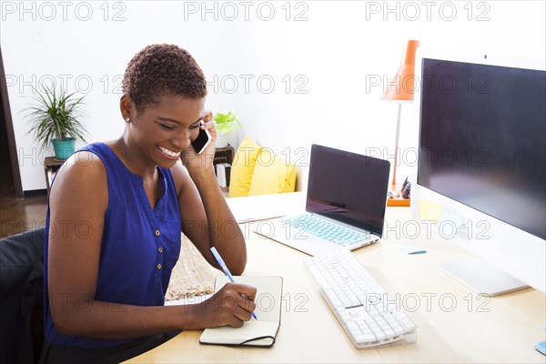 Black businesswoman talking on cell phone at office desk