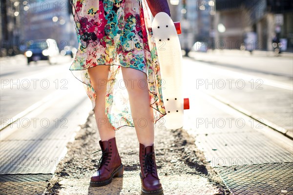 Woman carrying skateboard on city sidewalk