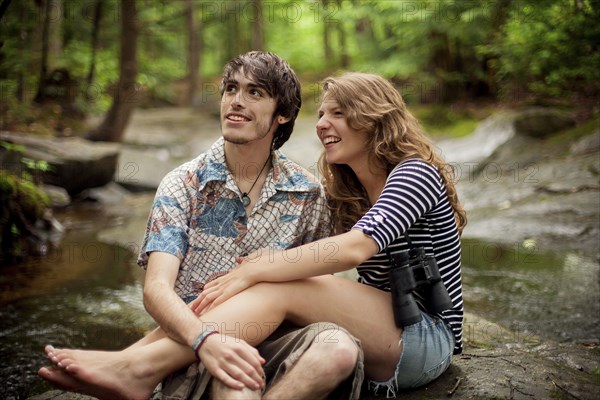 Couple sitting barefoot on boulders in forest