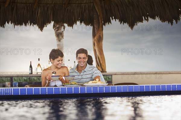 Hispanic couple having dinner at poolside