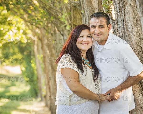 Older Hispanic couple hugging near tree