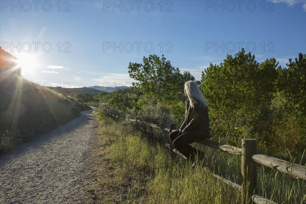 Older Caucasian woman sitting on wooden fence near mountain