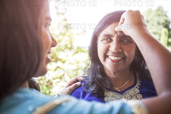 Indian woman putting jewel on mother's forehead