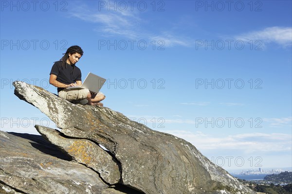 Man using laptop on rock