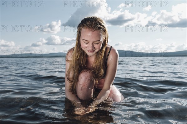 Caucasian teenage girl kneeling in ocean