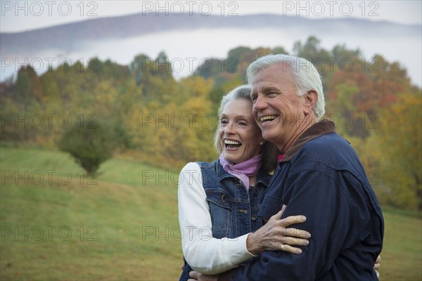 Older Caucasian couple hugging in field