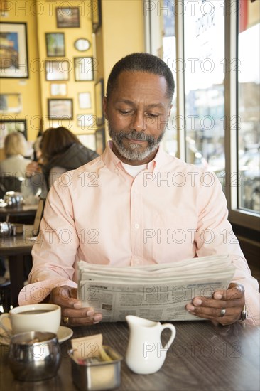 Mixed Race man reading newspaper in coffee shop