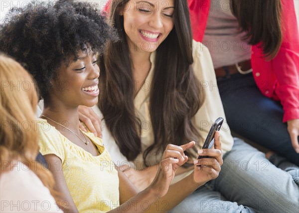 Women using cell phone together on sofa