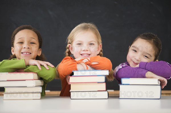Girls leaning on stacks of books in classroom