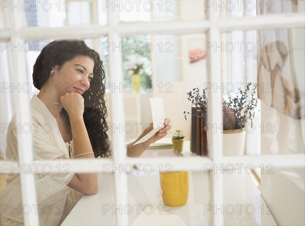 Mixed race woman reading card near window