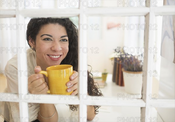 Mixed race woman drinking cup of coffee near window