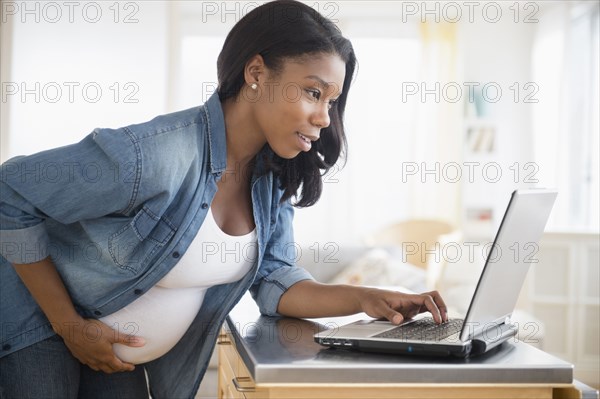 Black pregnant woman using laptop in kitchen